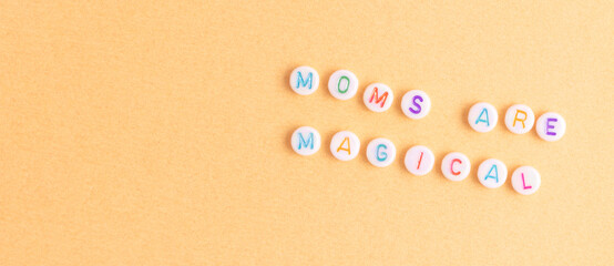 Moms are magical. Banner with quote made of round beads with letters on a gold colored background....