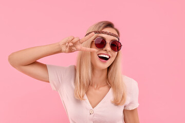 Portrait of smiling hippie woman showing peace sign on pink background