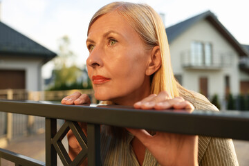 Concept of private life. Curious senior woman spying on neighbours over fence outdoors