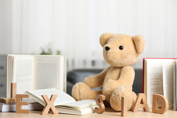 Dyslexia problem. Teddy bear, letters and open books on wooden table indoors