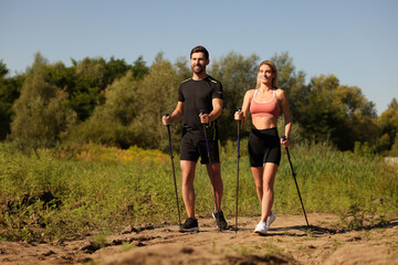 Happy couple practicing Nordic walking with poles outdoors on sunny day