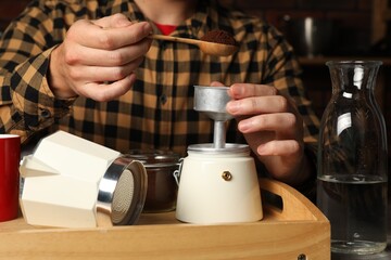 Man putting ground coffee into moka pot at table indoors, closeup