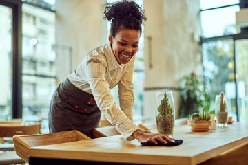 A smiling female African waitress cleaning a table, working in the morning.