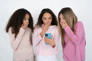 multi racial group of girl friends being deeply surprised, stares at smartphone display, reads...