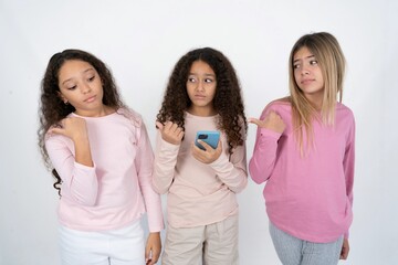 multi racial group of girl friends points thumb away and shows blank space aside, holds mobile phone for sending text messages.