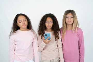 Upset dissatisfied multi racial group of girl friends uses mobile software application and surfs information in internet, holds modern mobile hand