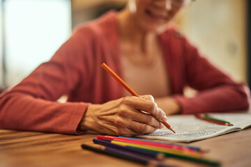 An older woman using a crayon and coloring the coloring book, close-up of the hand.