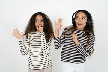 Happy multi racial group of girl friends sings favourite song keeps hand near mouth as if microphone wears wireless headphones, listens music