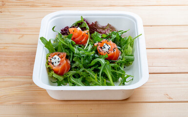 Salad with salmon, cream cheese and arugula. Healthly food. Takeaway food. On a wooden background.