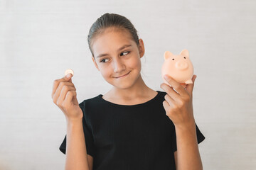 Happy excited teen girl saving money, dropping coin into pink piggy bank, cheerful female teenager...