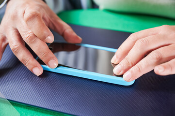 Protective screen for smart device. Unrecognizable woman using blue frame to align and center a screen protector while installing it on a mobile phone.