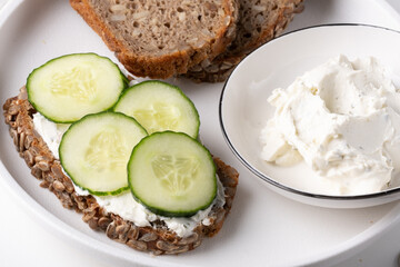 Rye bread with cream cheese and cucumbers on a white table. Whole grain rye bread with seeds