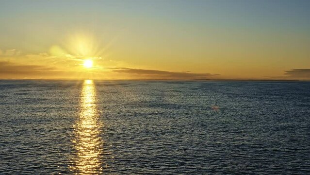 Sunrise at sea from sundeck of cruise ship side view. Morning sun, sunbeams and lens flare reflecting on sea surface with calm waves. On the horizon the coast of Norway voyage sailing travel concept