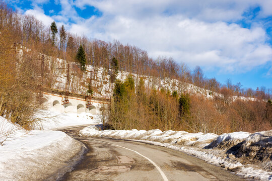 road pass winding through forested snow covered hills. mountainous winter landscape on a sunny day beneath a blue sky with clouds