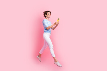 Full size profile photo of excited nice girl jump use smart phone empty space ad isolated on pink...