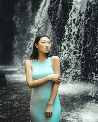 Portrait of Asian woman posing near the waterfall. Nature and environment concept. Travel lifestyle. Young woman wearing light blue dress. Copy space. Yeh Bulan waterfall in Bali