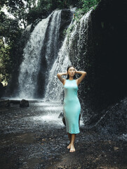 Attractive Asian woman posing near the waterfall. Nature and environment concept. Travel lifestyle. Woman wearing light blue dress. Slim body. Copy space. Yeh Bulan waterfall in Bali