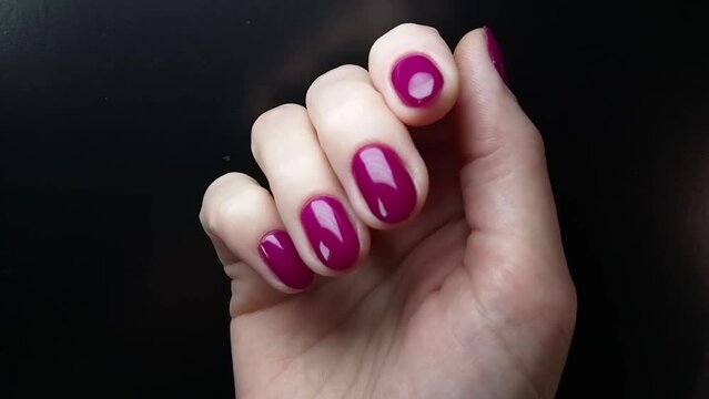 Nail art and glamorous manicure. A woman shows her nails painted with bright purple gel polish. Female hand close-up view at the black background