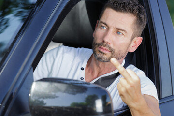 driver man in car smiling and showing sign middle finger