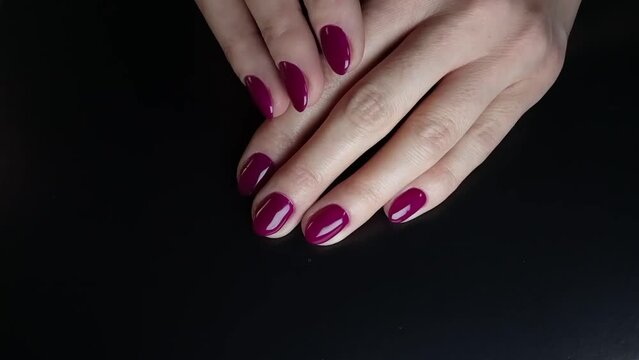 Nails care. Female hands with a rich purple color manicure on a black table. Smooth, slow motion of one palm over the other. Creative video for advertising gel nail polish, nail topcoat, beauty salon
