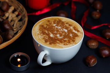 Cup of coffee with cinnamon, surrounded by chestnuts and a small perfumed candle, during winter and holiday season