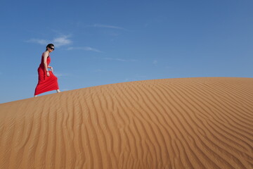 Fototapeta na wymiar Woman in red dress on sand dunes 