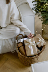Woman's hand takes a gift from a basket. New Year's mood in the house. Stylish interior with white sofa