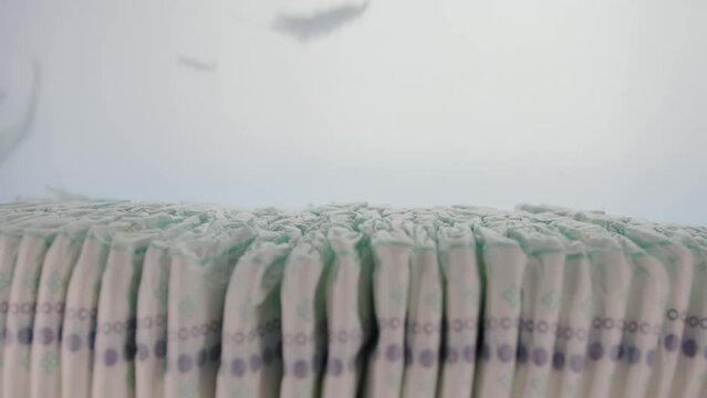 Stack of baby diapers with light feathers on a white background. Concept of lightness, softness and comfort when wearing diapers. Cotton. Copy space for text, slow motion