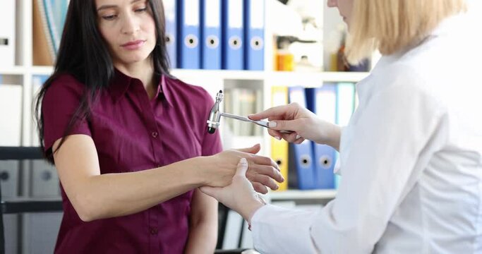 The doctor checks the reflex of the woman's hand with a hammer, close-up. Neurologist consultation, diagnostics