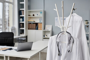 Medium close up of lab coats and stethoscope in doctors office, working desk and medical equipment...