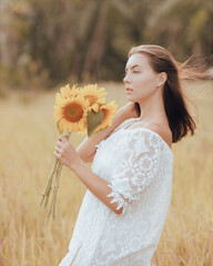 Close up portrait of attractive Caucasian woman holding sunflowers. Nature and outdoor concept. Summer time. Beautiful face profile. Woman touching her hair.