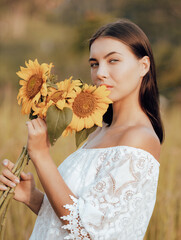 Close up portrait of charming woman holding sunflowers. Nature and outdoor concept. Summer time. Beautiful face. Sunset time.