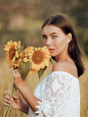 Close up portrait of attractive woman holding sunflowers. Nature and outdoor concept. Summer time. Beautiful face. Sunset time.