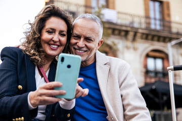 Cheerful mid adult couple having fun together taking a selfie in the street. Romantic senior couple smiling taking picture together in european city.