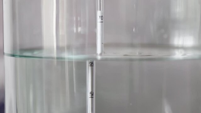 alcohol distilling process closeup - liquid distilled transparent liquid flowing in large glass jar with floating alcoholometer in it.