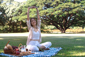 Beautiful young woman picnic on green grass on a sunny summer day, sit on a blanket and stretch...