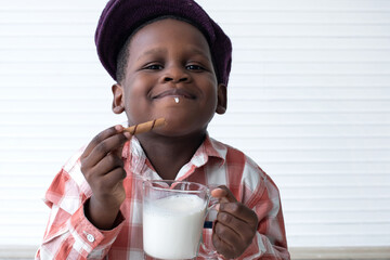 Happy African child enjoying dipping crisps into a glass of milk. and eat it deliciously, in white...