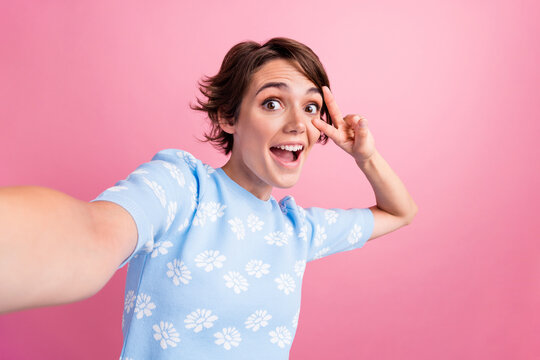 Photo of funky cheerful person take selfie demonstrate v-sign near eye isolated on pink color background