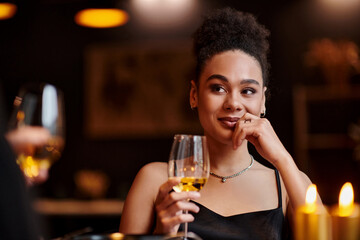 cheerful african american woman smiling and holding glass of wine during date on Valentines day
