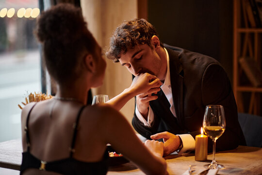 gentleman in elegant attire kissing hand of girlfriend during date in restaurant, Valentines day
