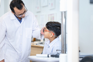 Fototapeta premium Indian child choosing eyeglasses in optics store, Boy doing eye test checking examination with optometrist in optical shop, Optometrist doing sight testing for child patient in clinic