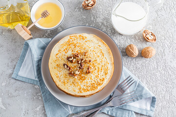 Delicious pancakes with honey and walnuts on a plate next to a jar of honey and nuts. Top view. Traditional breakfast for Maslenitsa.