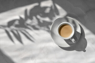 White ceramic saucer and cup with coffee drink on neutral marble gray table background with...