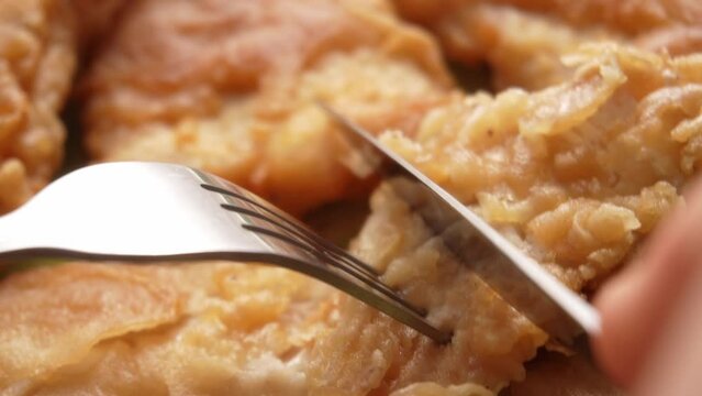 A fork lifts a flaky piece of fried fish, showcasing its crispy texture against more fillets in the background.