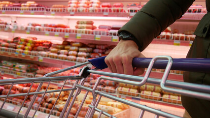 Close-up of the hand of a man rolling a shopping trolley in a sausages department