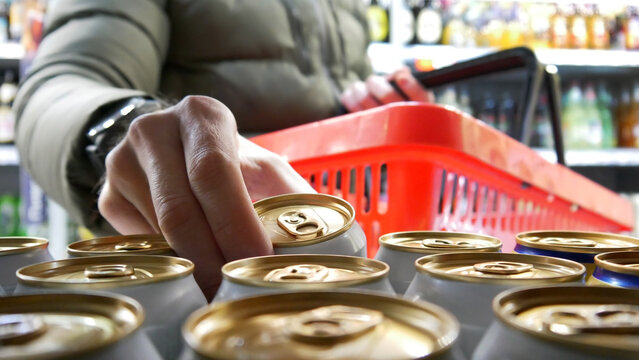 Close-up of the hand of a man with a shopping basket taking a golden-white can of beer in alcohol department