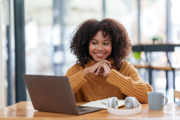Cheerful young african american woman using computer laptop in coffee shop.
