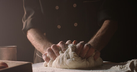 Hands of senior experienced chef kneading floured dough at bakery, old man making homemade bread...