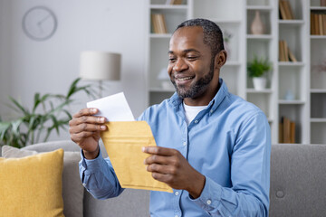 Senior joyful man sitting on sofa at home, satisfied smiling african american man reading mail...
