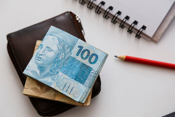 one hundred reais notes and other notes on the table with wallet, pencil and notebook